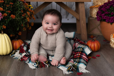 Photo of a little boy against a fall background of mums, pumpkins, and flannel