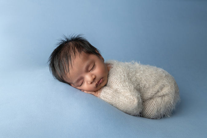 newborn baby boy in ivory pjs sleeps against light blue backdrop