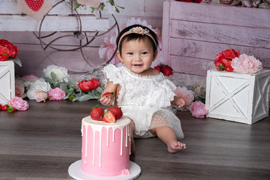 Smiling baby girl in a white dress with a strawberry cake