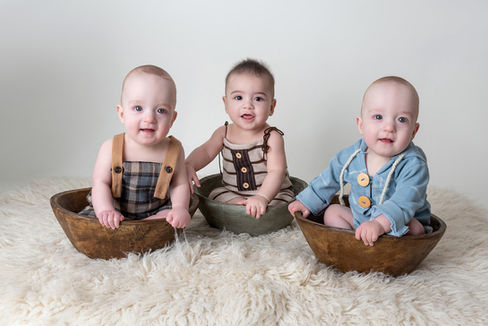 Triplet boys sitting in wooden bowls on a white shag rug