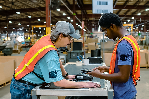 two warehouse employees talking at a pack table, warehouse in the background