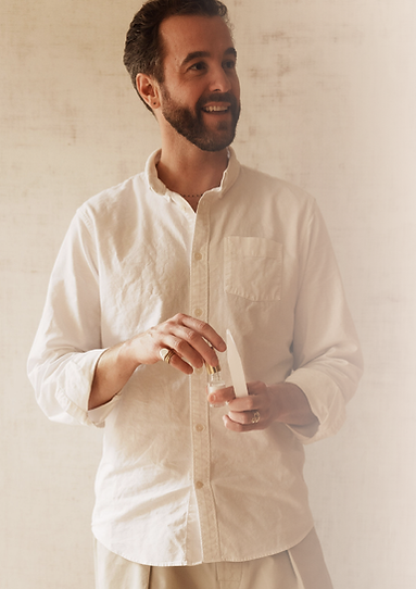 tim mcmullan Smiling holding a perfume tester, wearing a white shirt; smiling and looking away.
