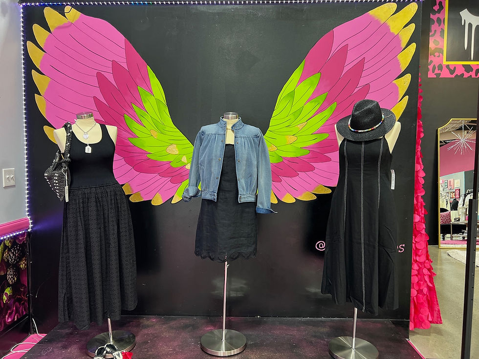Mannequins in black dresses and denim before pink wings.