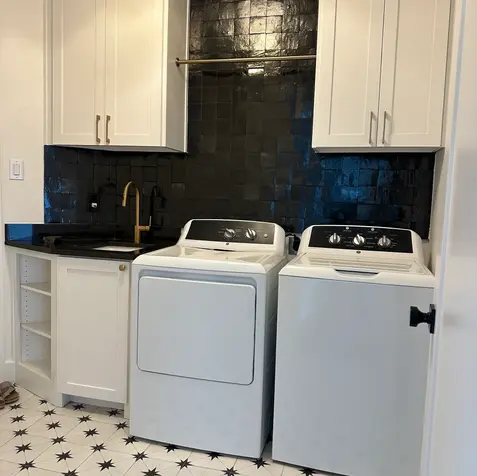 Laundry room with white washer and dryer, black backsplash, custom cabinets, and star-patterned floor tiles.