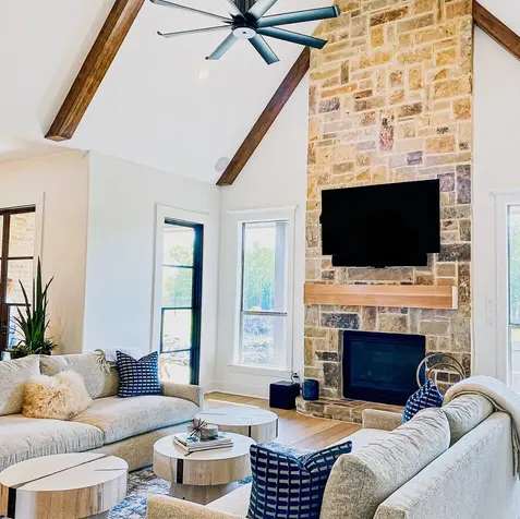 Living room features custom cabinets, two beige sofas, a stone fireplace, mounted TV, blue cushions, and rugs.