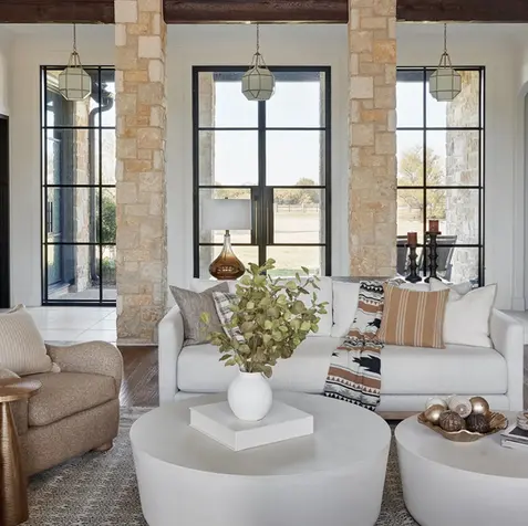Modern living room with white sofa, beige armchair, round coffee table, decorative vase, and large windows; perfect for home renovations.