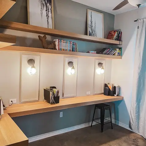 Modern study nook with a wooden desk, black stool, wall lights, custom cabinets, framed art, a rug, and a ceiling fan.