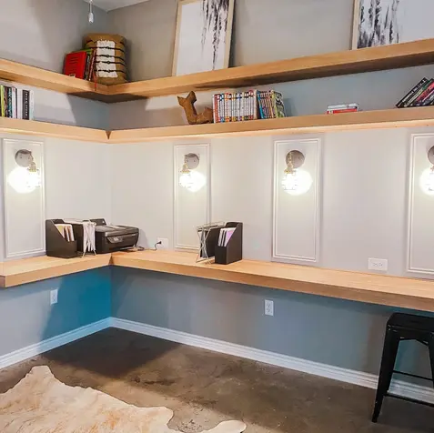 A modern office space with wooden shelves, wall-mounted lights, a printer, files, and a cowhide rug; perfect for home additions.