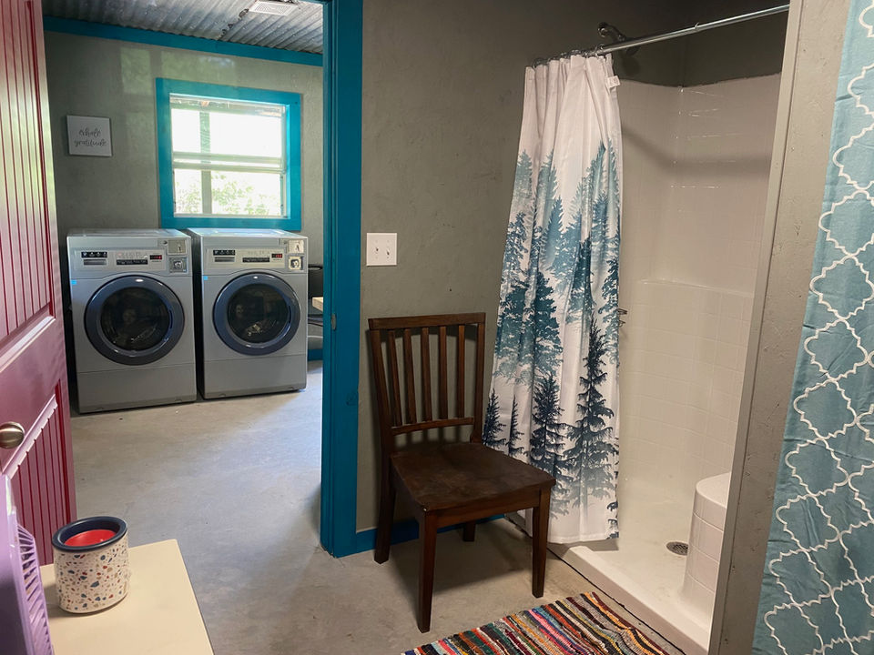 Laundry area with washer and dryer, shower, and a wooden chair.