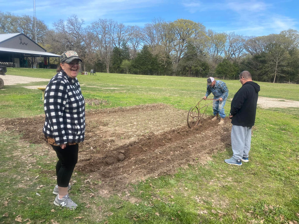 Three people working a garden on a sunny day with trees in background.