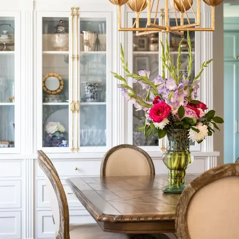 Dining room with a wooden table, floral centerpiece, and glass-front cabinet displaying decor—perfect for post-kitchen remodels.