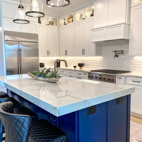 Modern kitchen with custom cabinets, stainless steel appliances, and a large blue island. Three pendant lights hang above.