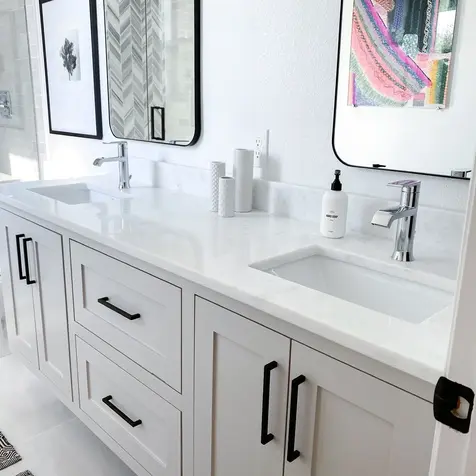 A modern bathroom remodel features a double sink vanity, black handles, wall-mounted square mirrors, and vibrant abstract art.
