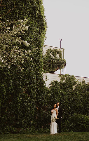 Photograph of a couple outside the Gatehouse wedding venue in the summer with lush greenery surrounding them.