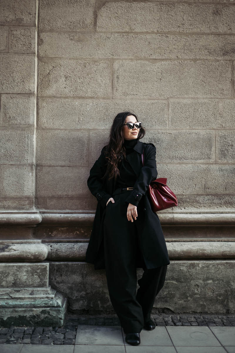 Дівчина в чорному з бордовою сумкою та чорними окулярами