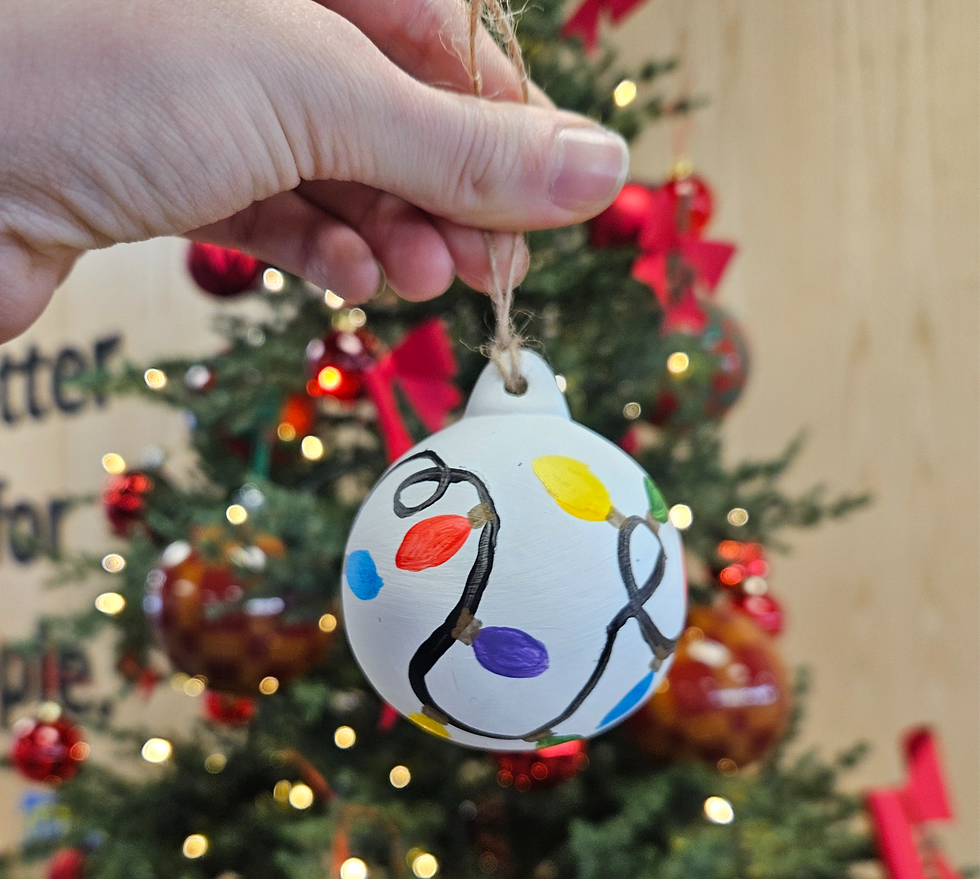 Hand hangs a white ornament painted with colorful Christmas lights on a decorated tree with red bows and warm lights
