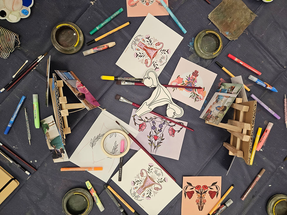 A table with lots of art supplies laid out including reference pictures of wombs, pens, paints, easle and examples.