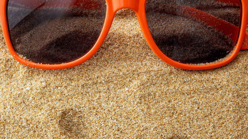 Orange sunglasses rest on sandy surface, forming a smiling face. Bright and playful beach theme with a cheerful mood.