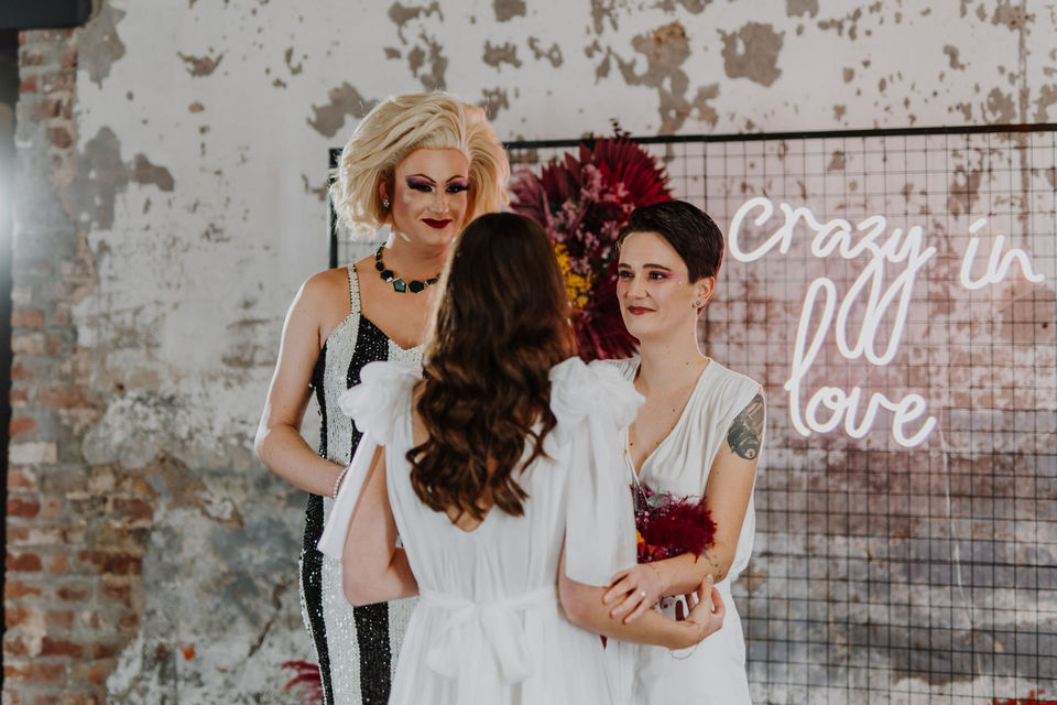 Queeres Paar während der Trauung mit Drag Queen bei ihrer 80er Motto-Hochzeit geplant von Hochzeitsplanerin Köln. // Queer couple during their ceremony with drag queen at their 80s themed wedding planned by wedding planner Cologne.