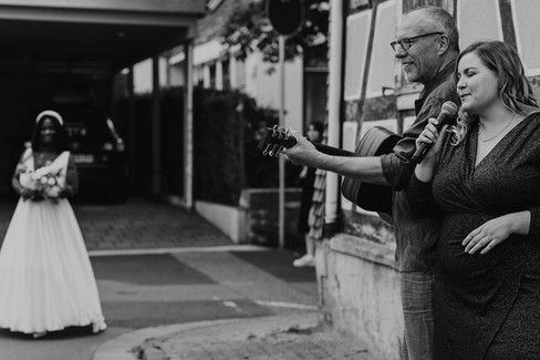 Eine Schwarze Braut vor der inklusiven Kirche mit weißen Musiker:innen vor der Hochzeit geplant von Hochzeitsplanerin Hessen. // A Black bride in front of the inclusive church with white musicians before wedding planned by wedding planner Hesse.