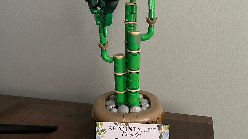 Lego bamboo plant on wooden surface with an appointment reminder card. Green and brown hues with a calm, organized setting.