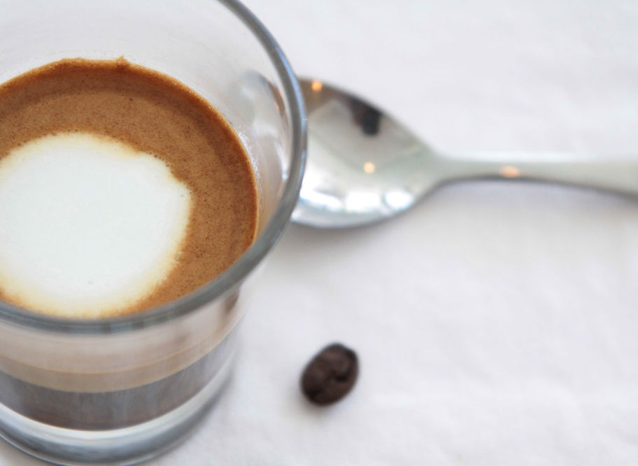 Espresso in glass with spoon and coffee bean on white background