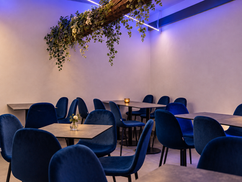 Tavoli e sedie blu sotto una trave decorata con piante e fiori, con un piccolo vaso sul tavolo in primo piano.