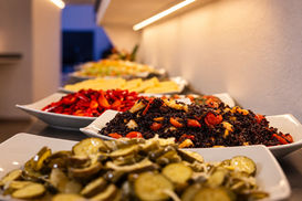 Primo piano dei vassoi del buffet con verdure e preparazioni assortite disposte lungo il bancone.