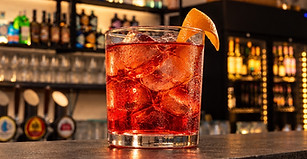 Cocktail rosso con ghiaccio e guarnizione d’arancia sul bancone del bar