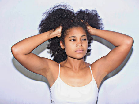 Black woman gently feeling her natural hair with both hands as she leans its texture and needs.