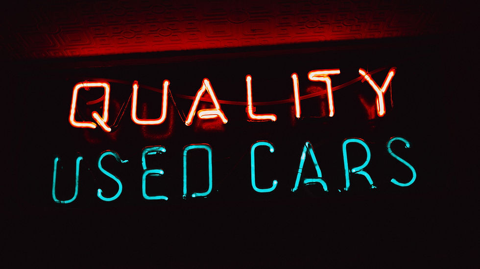 Neon sign reads "QUALITY USED CARS" in red and blue against a dark background, creating a retro, vibrant atmosphere.