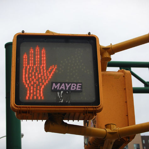 A cross walk signal with a stop hand and text that says "Maybe"