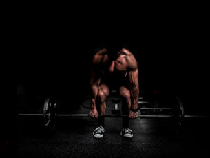 muscular man lifting weights. black background behind him. about to preform a deadlift pecks, traps, lats, strong athletic man