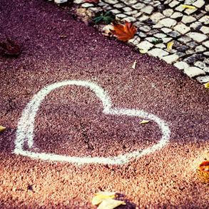 Corazón de tiza blanca en asfalto rojo, hojas de otoño dispersas, borde de adoquines. Ambiente otoñal y romántico.