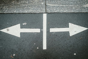White double arrows on textured gray pavement pointing left and right, divided by a vertical line. Urban setting, worn surface