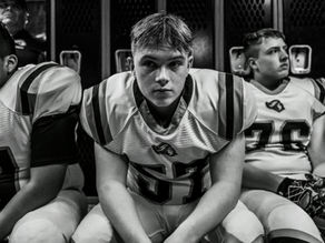 Three football players sitting in a locker room bench