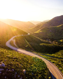 Winding road through sunlit mountain valley at golden hour. Image by Matt Howard