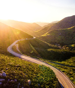 Winding road through sunlit mountain valley at golden hour. Image by Matt Howard