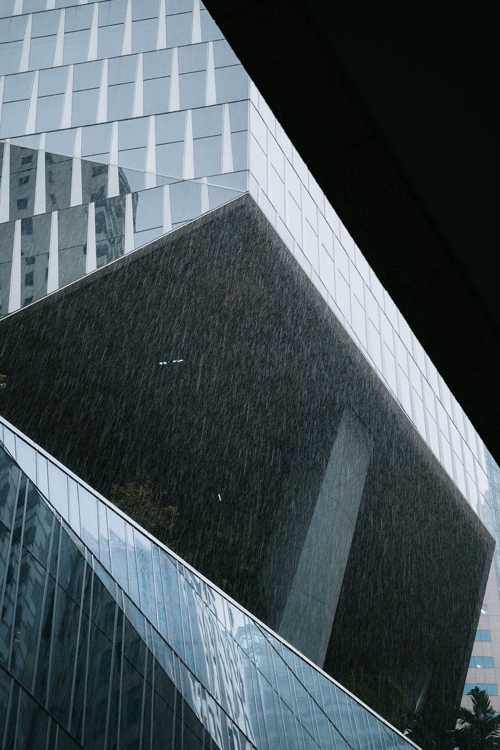 倾斜角度拍摄的现代建筑,几何图案窗户,细雨中,大气而冷峻的氛围。背景为城市高楼。