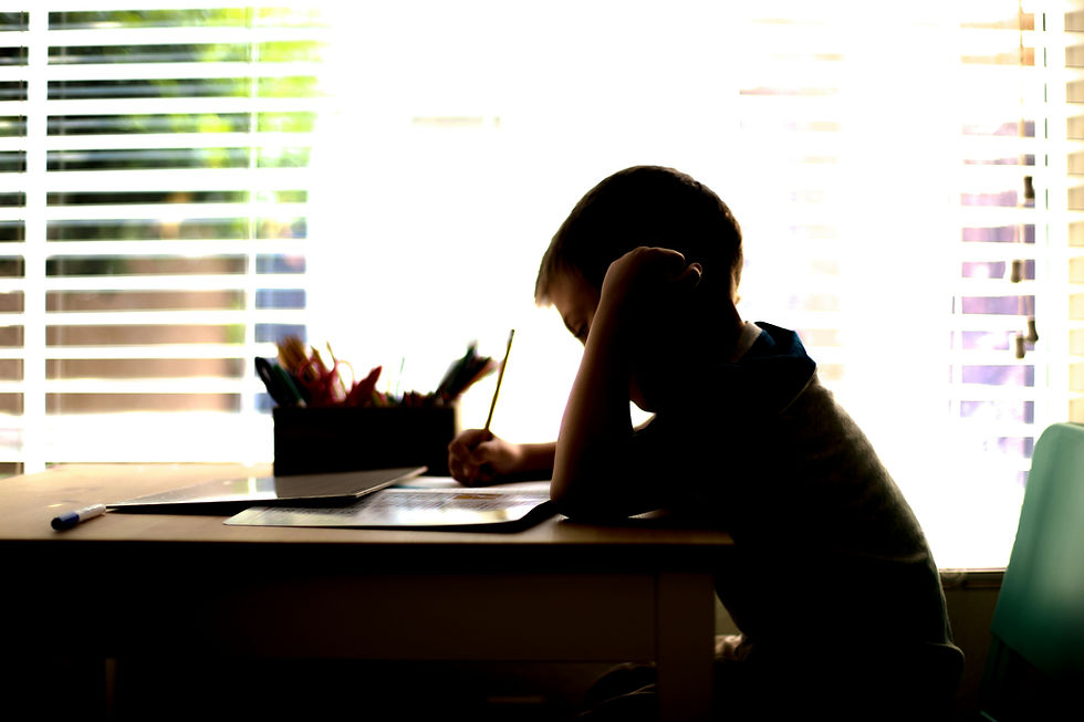 A silhouette of a child working homework at a day. The child's arm is up with their head resting on their fist.