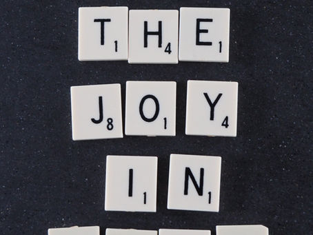 Scrabble tiles on a dark surface spell "HEAR THE JOY IN LIFE" in black letters, creating an uplifting message.