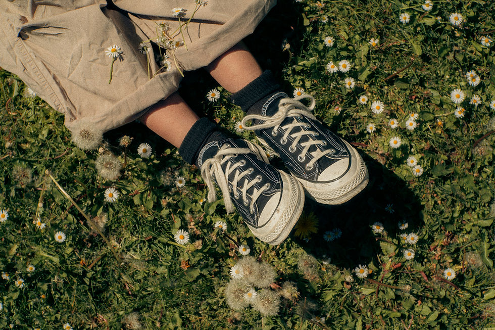 Legs in a beige skirt, black socks and sneakers lying in a field of tiny white daisies and dandelions.