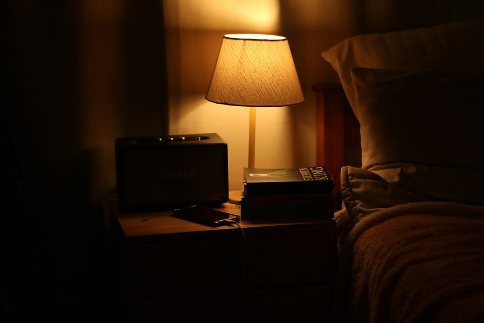 Dim bedroom with soft bedding and a warm glowing lamp on a nightstand creating a calm nighttime atmosphere for winding down before sleep