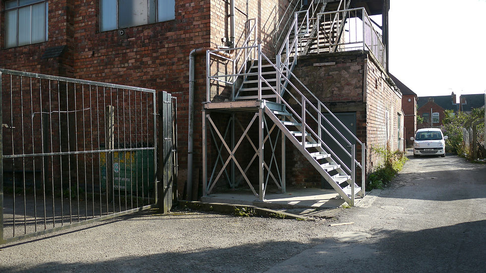 Exterior view of a brick industrial building with a metal staircase and a closed gate