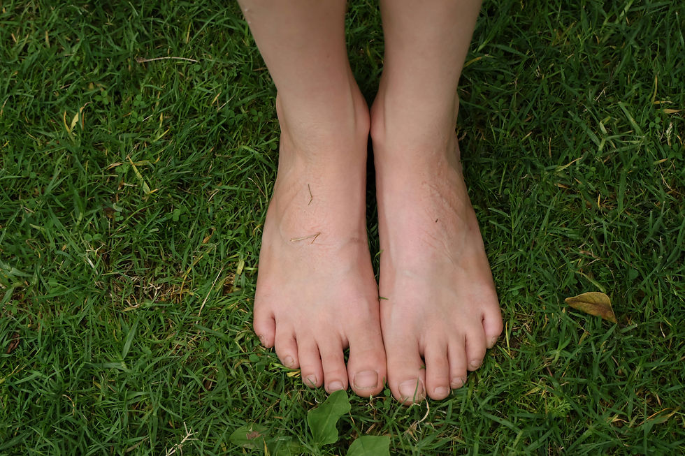 Bare feet standing on green grass with small leaves scattered. The setting is outdoors, conveying a sense of relaxation and nature.