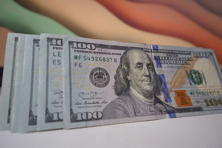 Fanned stack of U.S. $100 bills with Benjamin Franklin visible, laid on a white surface.