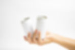A hand holds two blank white cans against a plain white background, emphasizing simplicity and minimalism.