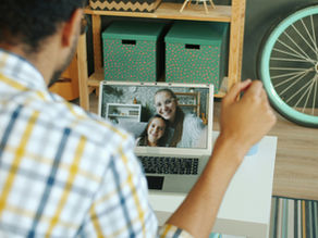 A man on a video call smiling warmly at his wife and daughter on the screen, symbolizing the emotional connection and joy of staying in touch despite living apart in a long-distance relationship.