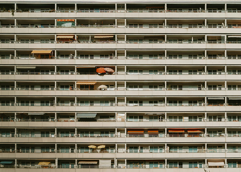 High-rise apartment building with rows of balconies featuring various awnings and umbrellas in muted colors. No visible people, neutral mood.