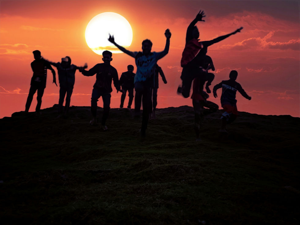 Silhouettes of people jumping joyfully on a hill during sunset. The sky is vivid orange with a large sun, creating an energetic mood.